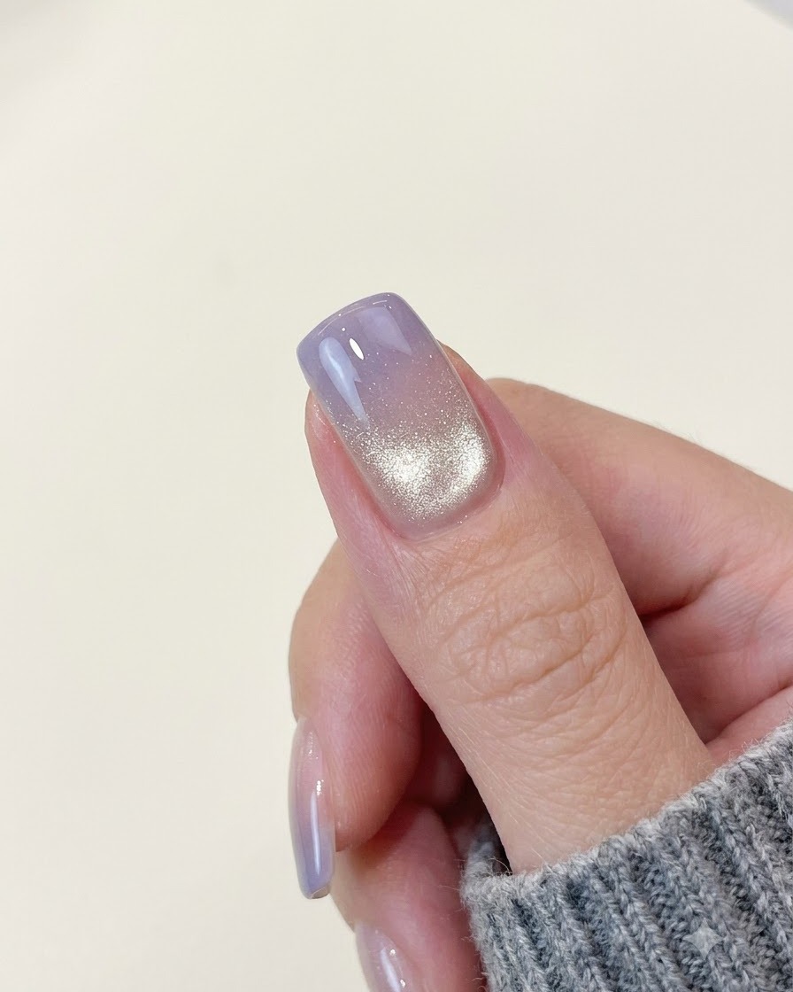Un ongle terminé avec un dégradé violet effet œil de chat montrant une bande de lumière scintillante brillante près du bord arrière.