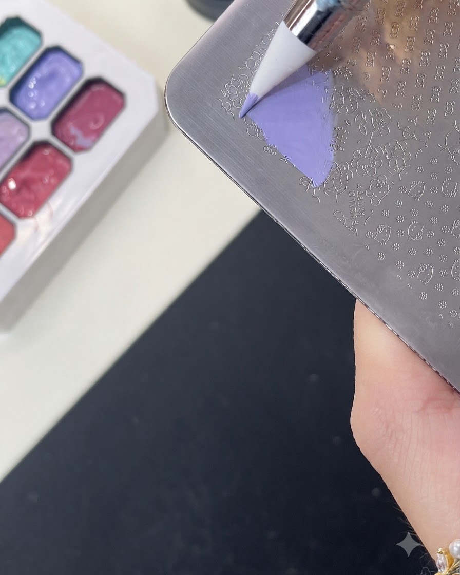 Un pinceau appliquant du gel de couleur violette sur un motif Hello Kitty gravé sur une plaque de stamping en métal.
