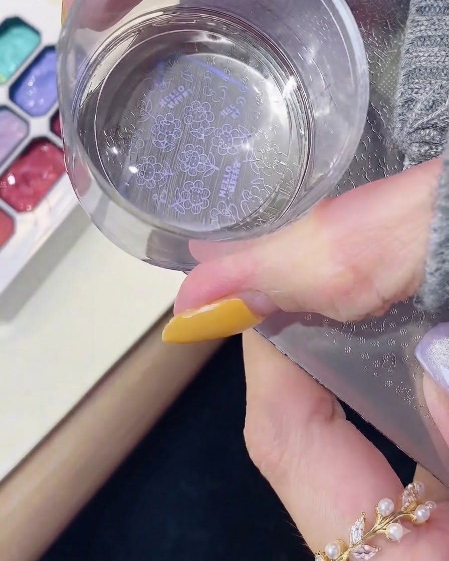 Un tampon en silicone transparent pressant vers le bas sur une plaque de stamping en métal pour récupérer un motif Hello Kitty violet.