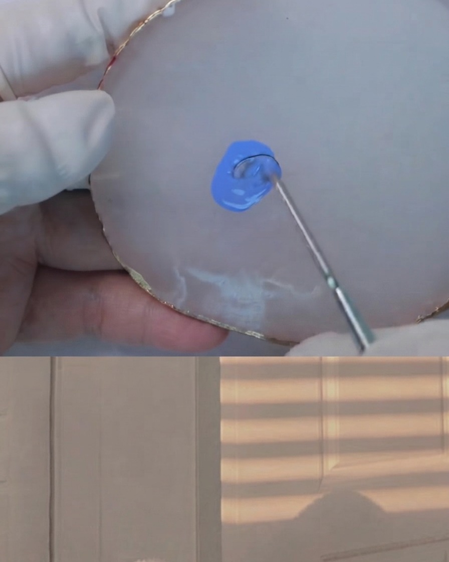 Un outil de mélange incorporant une quantité infime de gel foncé dans un mélange de bleu clair sur une palette en agate blanche.