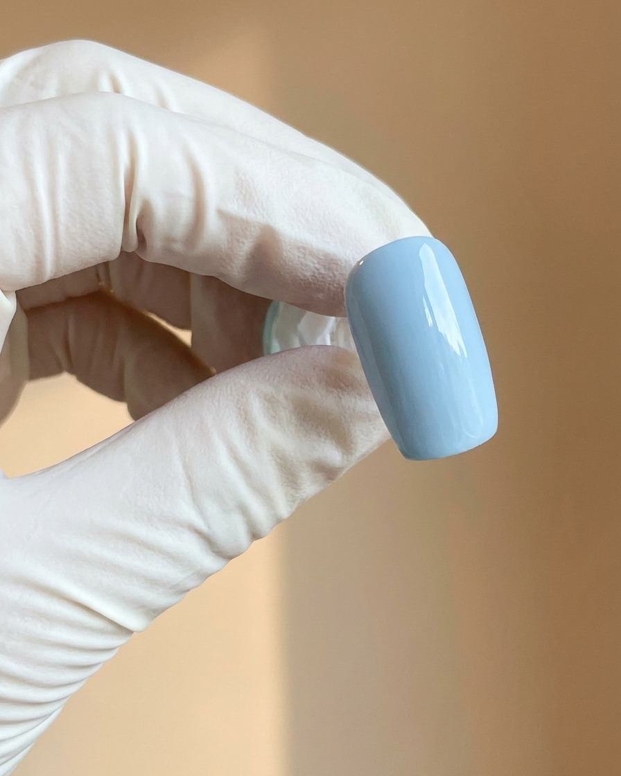 Une main gantée tenant un ongle bleu clair doté dune finition mate lisse.