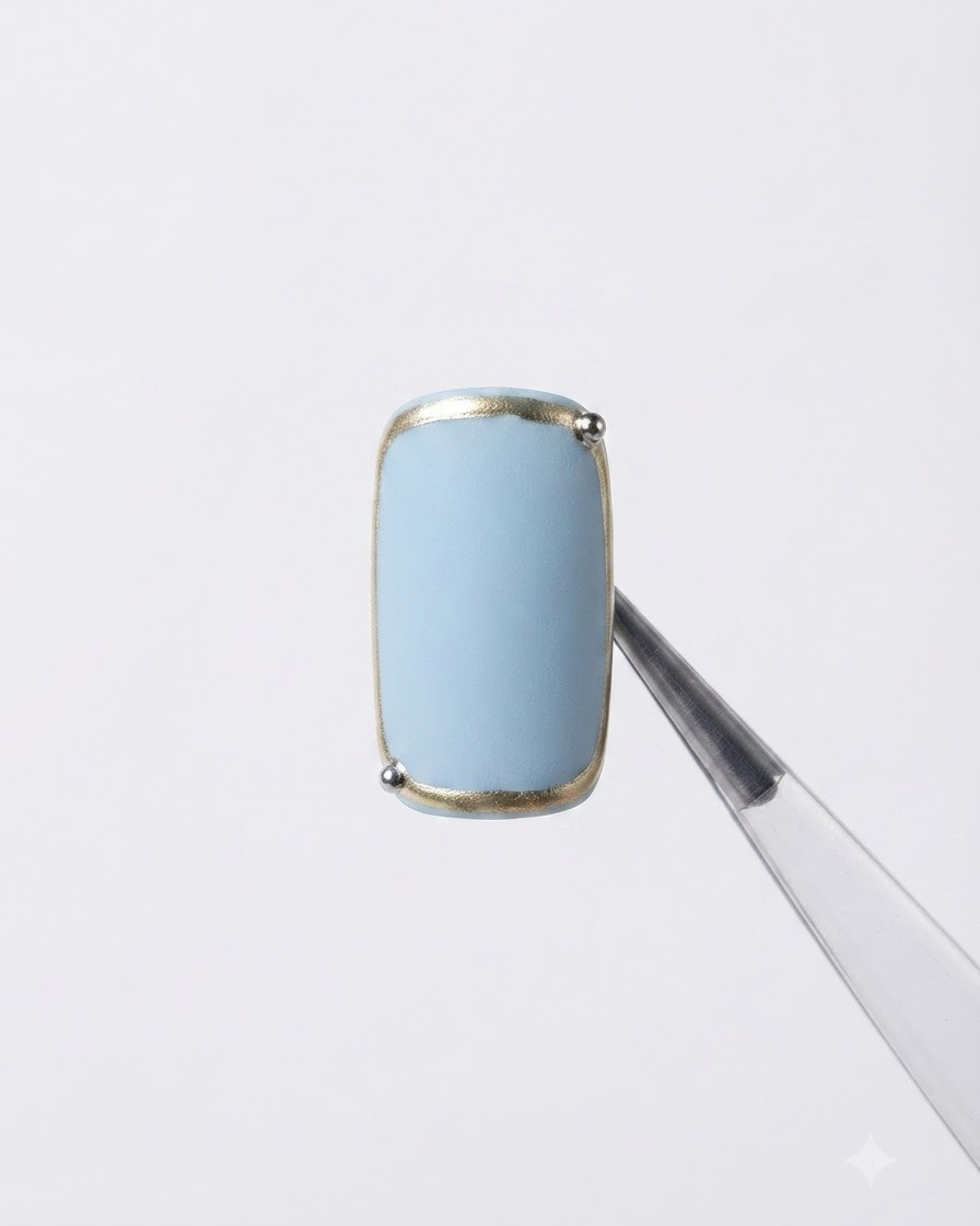 Un ongle tenu avec une pince à épiler présentant une bordure de cadre métallique finie et une minuscule bille argentée dans le coin.