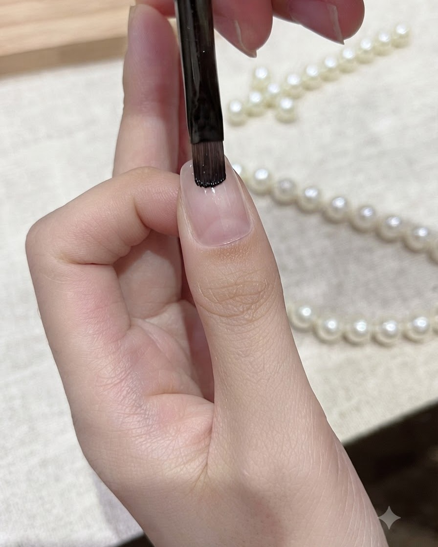 Un pinceau à gel plat appliquant du vernis gel noir directement sur le bord libre dun ongle naturel.