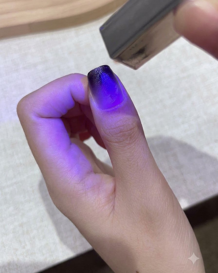 Une petite lampe UV/LED violette portable catalysant un design en gel dégradé sur un ongle de pouce.