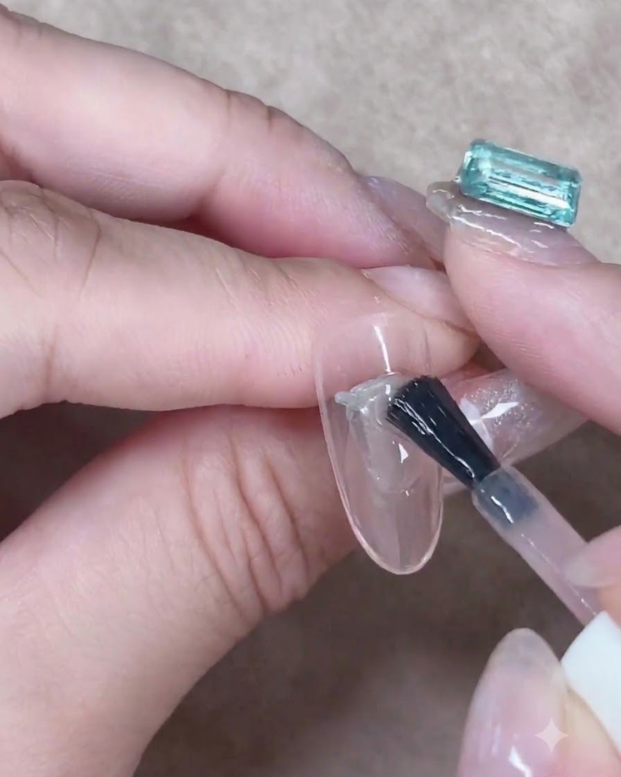 Un pinceau à gel lissant soigneusement une couche de gel nude translucide au centre dun ongle en amande.