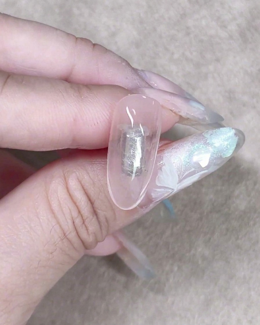 Une petite éponge à maquillage tapotant délicatement un gel laiteux transparent sur un onglet pour créer un fond texturé doux.