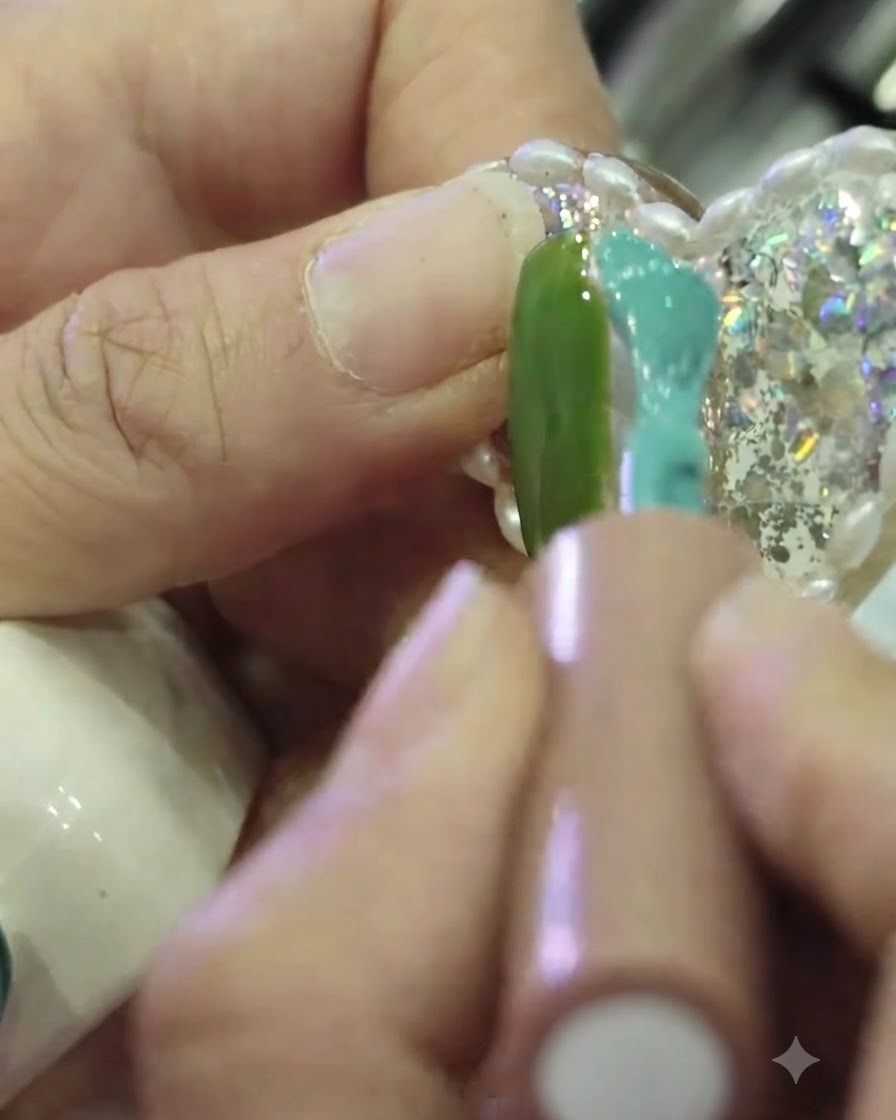 Gros plan dun pinceau à ongles appliquant du vernis gel teal sur le côté droit dun ongle, le côté gauche étant peint en vert, laissant une fine bande non peinte au centre.