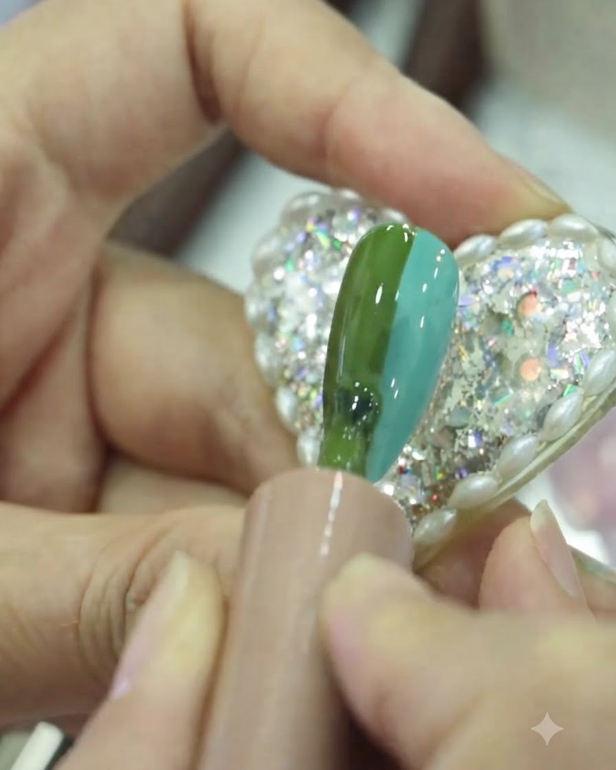Un pinceau plat estompant délicatement la section médiane où le gel vert et le gel teal se rejoignent sur longle.