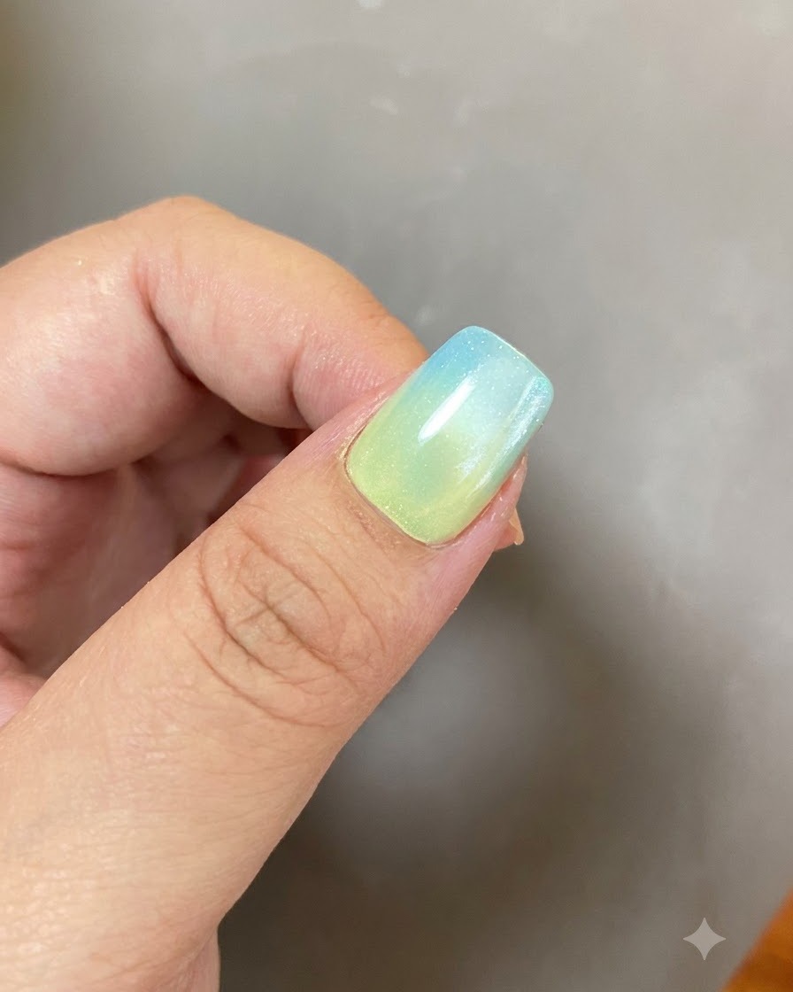 Une manucure en gel terminée avec un dégradé bleu-jaune et un design danneau lumineux sous un éclairage doux.