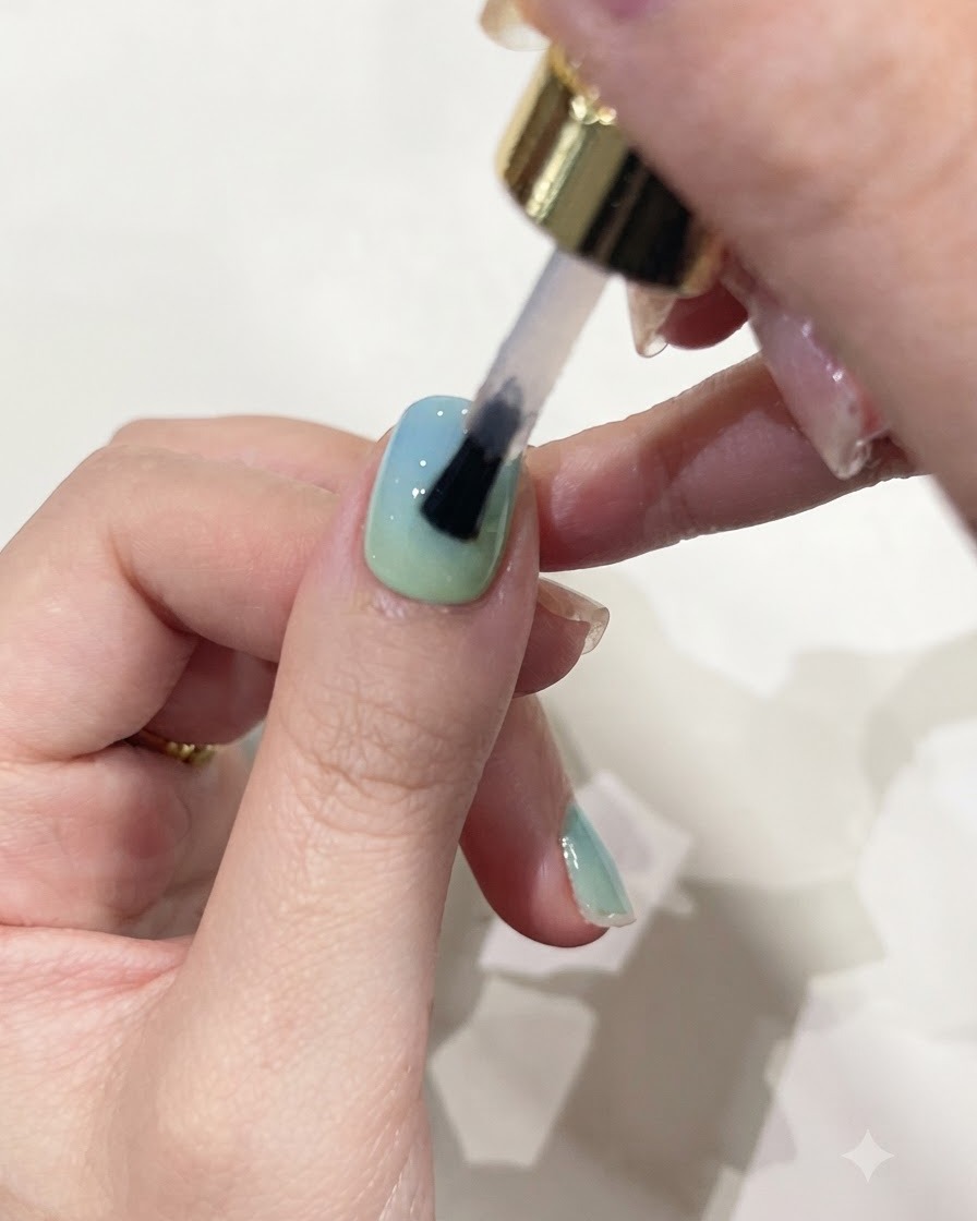 Un pinceau appliquant du gel de construction transparent sur un ongle aux couleurs dégradées.
