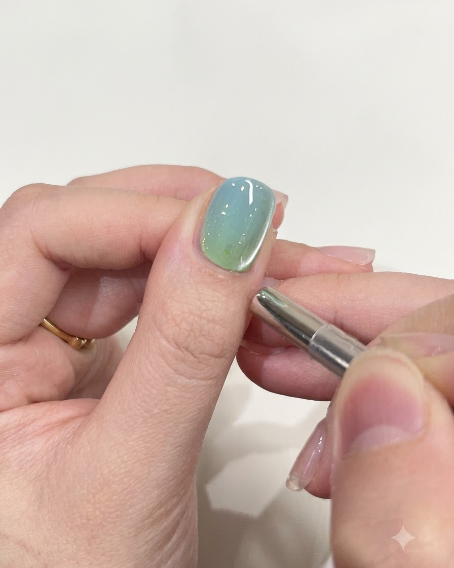 Un petit outil magnétique cylindrique placé à proximité du bord dun ongle peint avec du gel brillant.