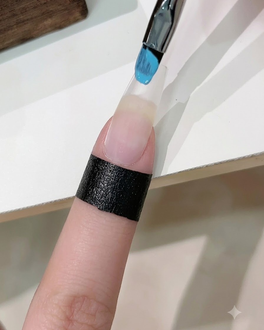 Une éponge chargée de vernis gel bleu et blanc tamponnant un dégradé sur un faux ongle rallongé.