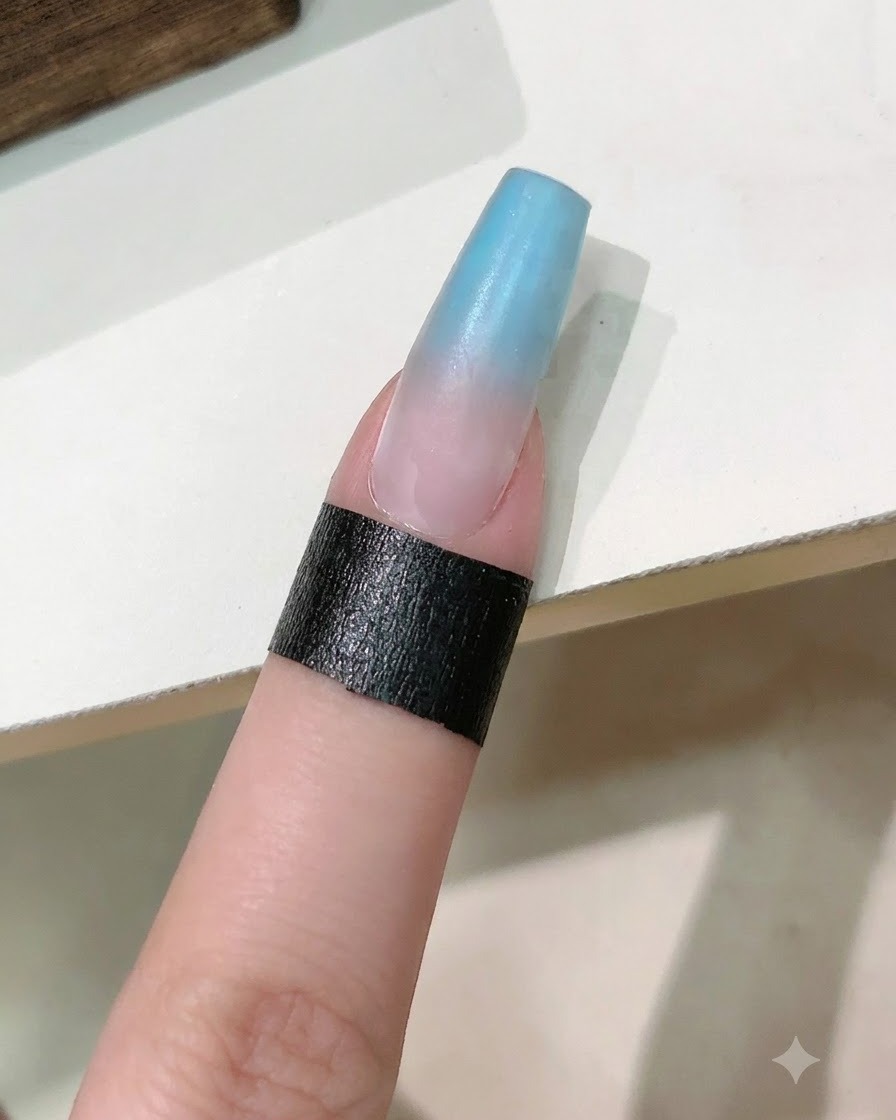 Un pinceau appliquant une couche de gel de renfort transparent sur longle dégradé bleu et rose.