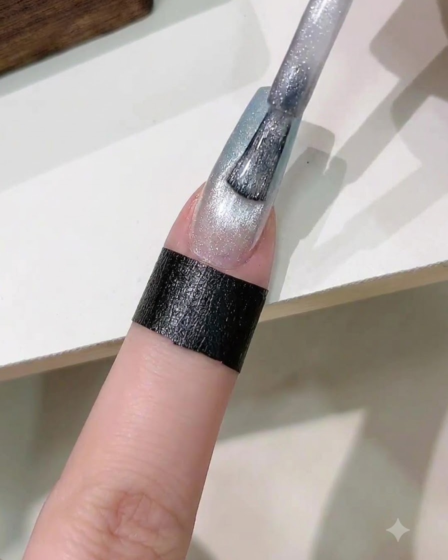 Un pinceau appliquant une couche de vernis gel magnétique cat eye argenté sur longle dégradé.