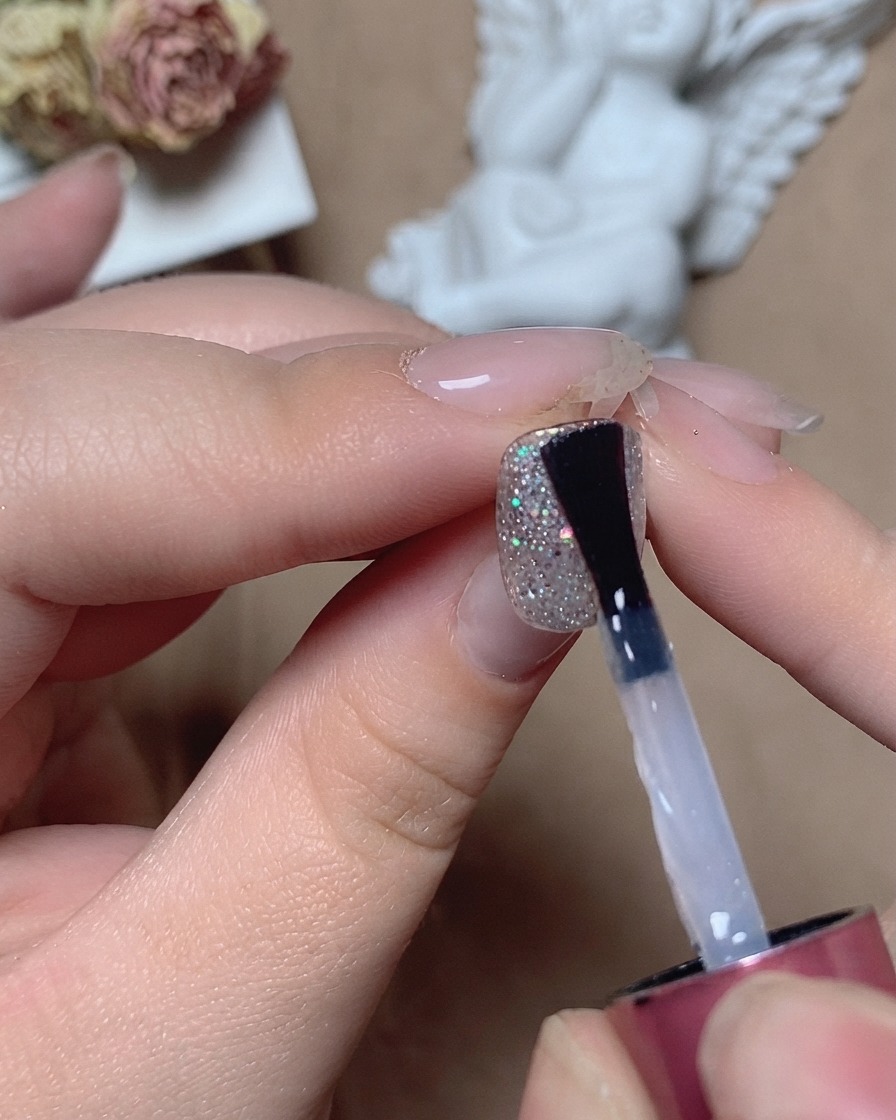 Un pinceau appliquant un top coat égalisateur transparent sur un ongle pailleté texturé sous un éclairage de studio.