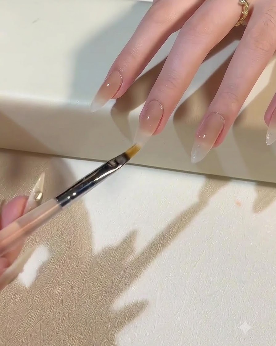 Un pinceau appliquant un gel blanc laiteux pour créer un dégradé ombré vers le bas de longle.