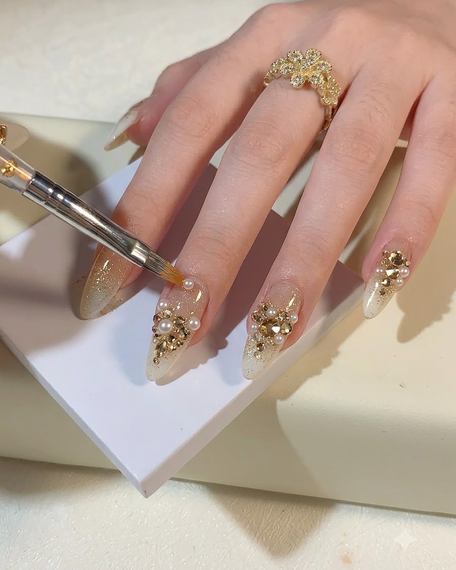 Un pinceau de détail ou un outil plaçant de petites perles et des strass or champagne sur un ongle pailleté.
