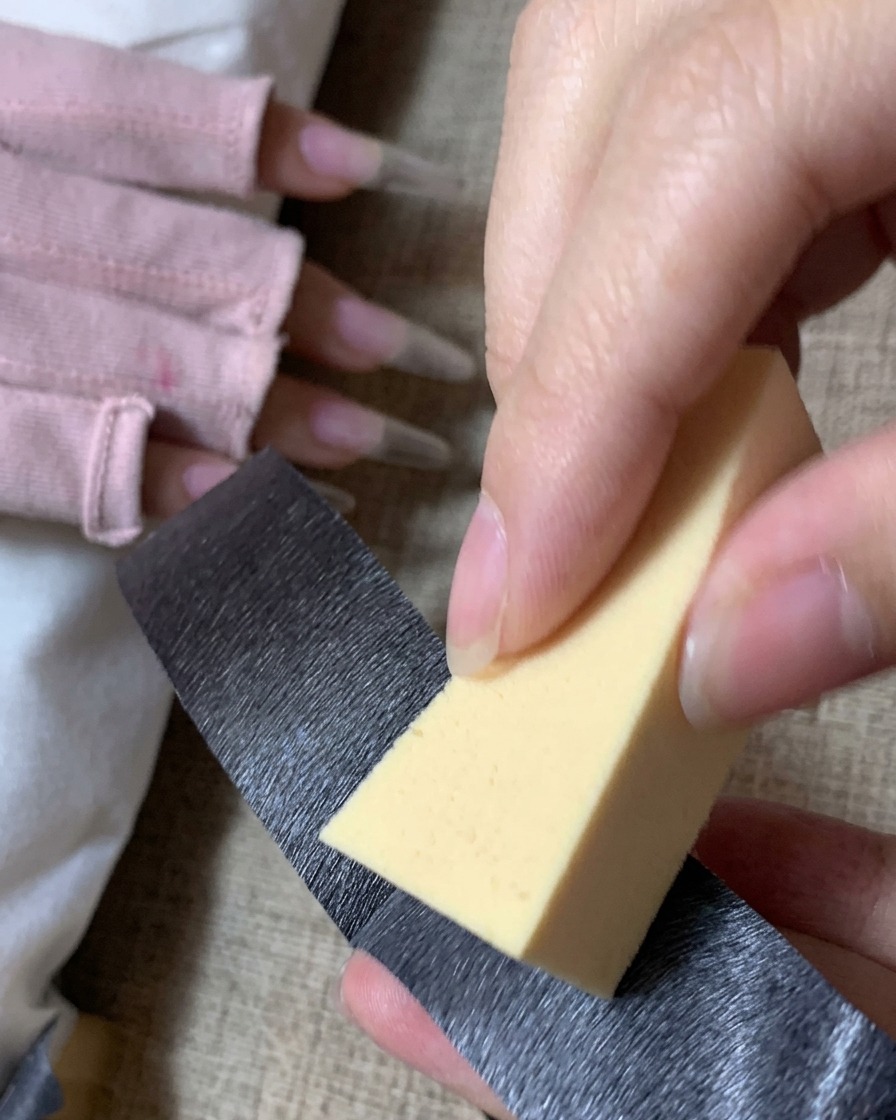 Une personne utilisant du ruban adhésif noir pour nettoyer la poussière dune éponge de maquillage triangulaire jaune.