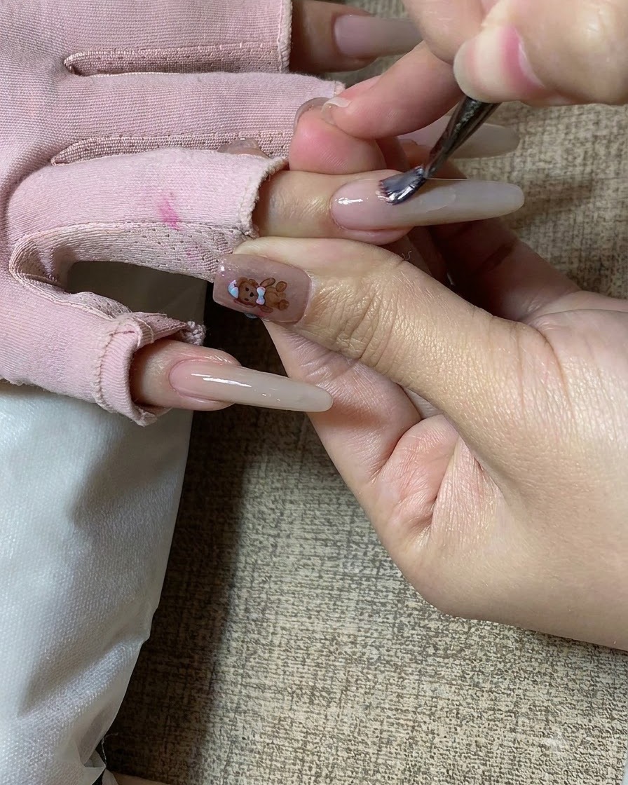 Un pinceau à ongles appliquant du gel couleur thé au lait sur un ongle sculpté long.
