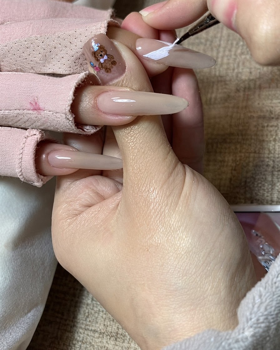 La main dune prothésiste ongulaire affinant les motifs dailes de papillon blanches sur un ongle allongé.