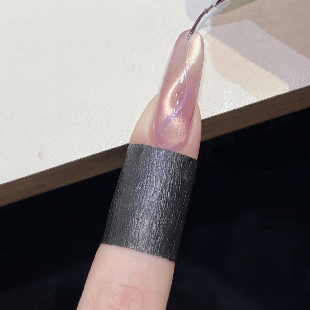 Un aimant cylindrique maintenu près dune ligne cat-eye violette sur un ongle rose scintillant.