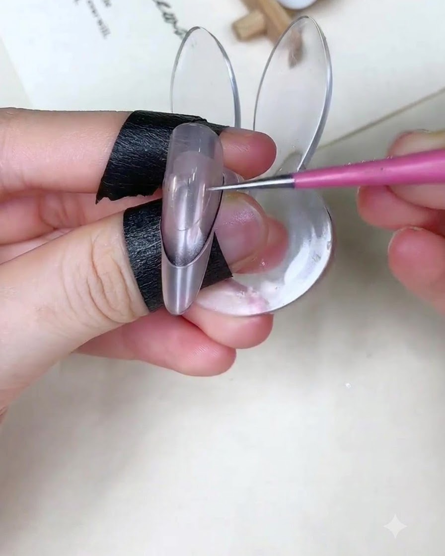 Un pinceau à ongle appliquant du gel bleu bébé sur la partie supérieure dun ongle par-dessus un sticker de guidage.