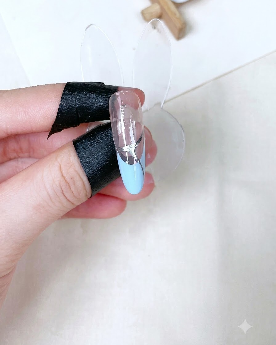 Un présentoir à ongle unique montrant un top coat transparent brillant catalysé avec des détails argentés sur une French bleu bébé.
