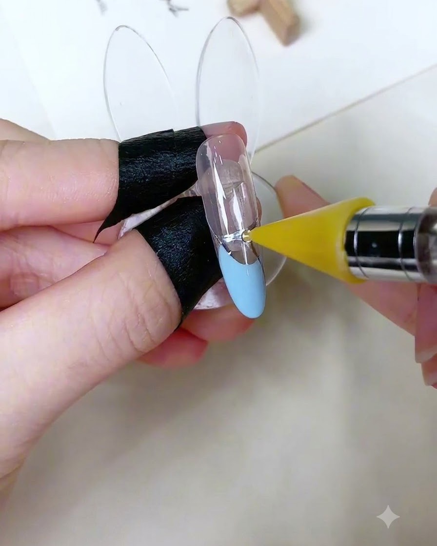 Un outil de préhension spécialisé positionnant un petit strass rond sur un point de gel adhésif dun ongle décoré.