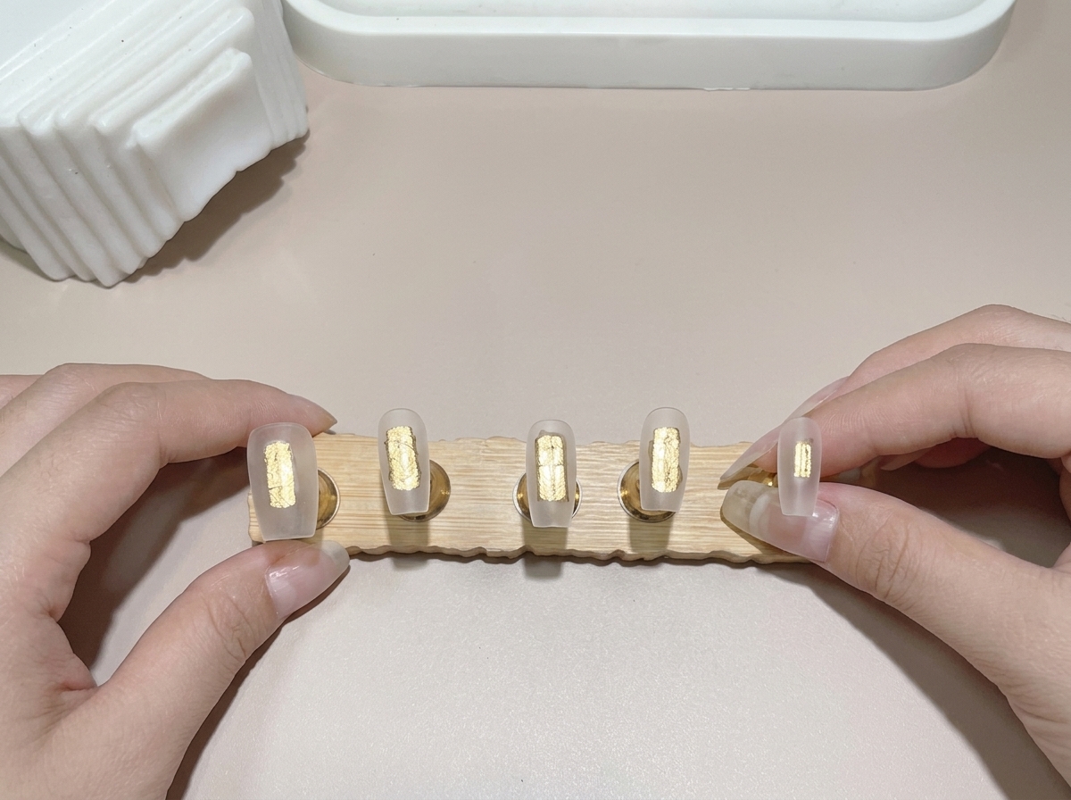 Gros plan dun pinceau appliquant du gel de base sur plusieurs capsules dongles fixées sur un support en bois.