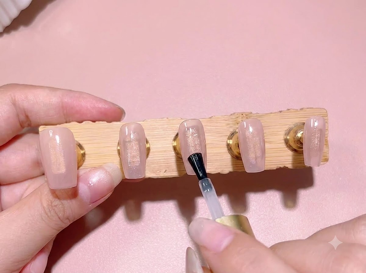Un pinceau de vernis classique appliquant une couche de gel blooming transparent par-dessus une couleur de base rose translucide sur un ongle.