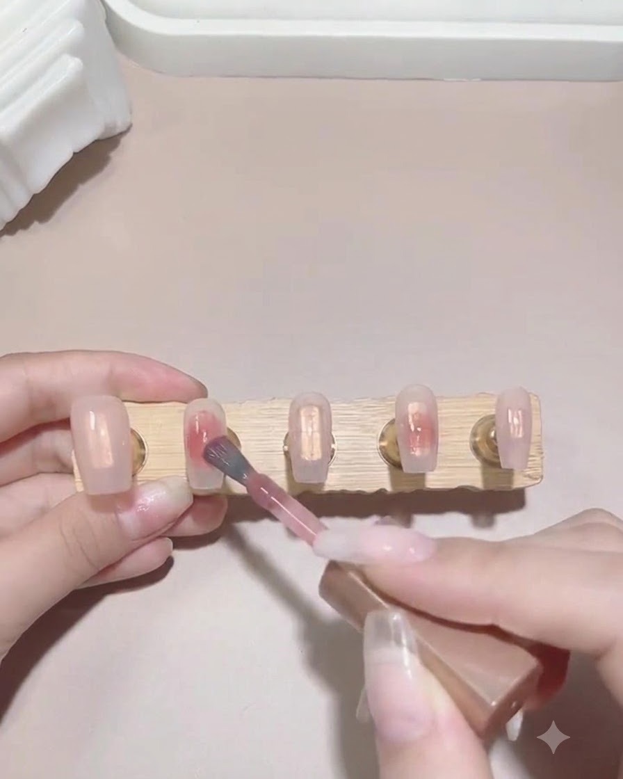 Un pinceau déposant une petite goutte de vernis gel rose sur la surface humide dune capsule dongle pour amorcer un effet dégradé.