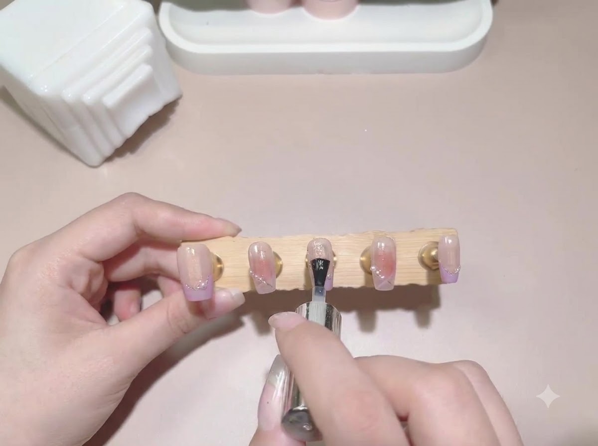 Un pinceau de top coat appliquant la finition sur un présentoir de faux-ongles peints et terminés.