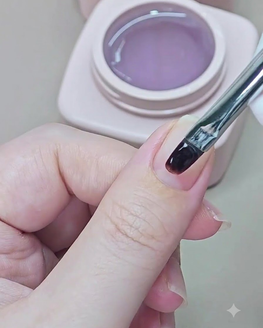 Un petit pinceau à ongle applique du gel de base transparent sur un ongle naturel.