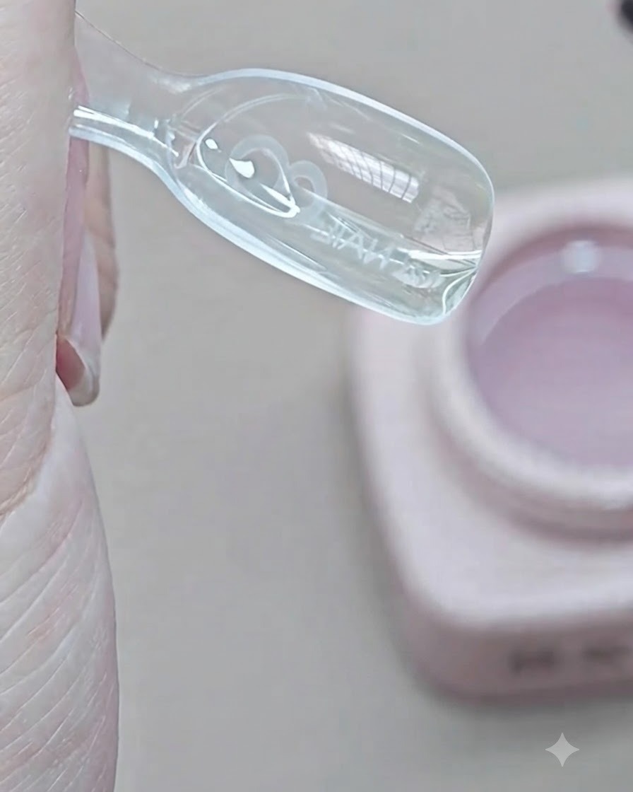 Un pinceau dépose du gel dextension transparent dans le creux intérieur dun moule dual form transparent.