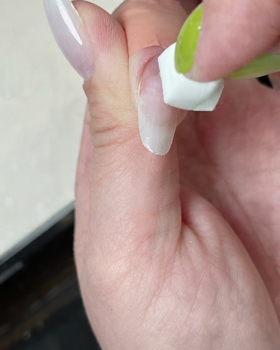 Un ongle en cours de catalysation sous une mini lampe avec une lueur de lumière blanche.