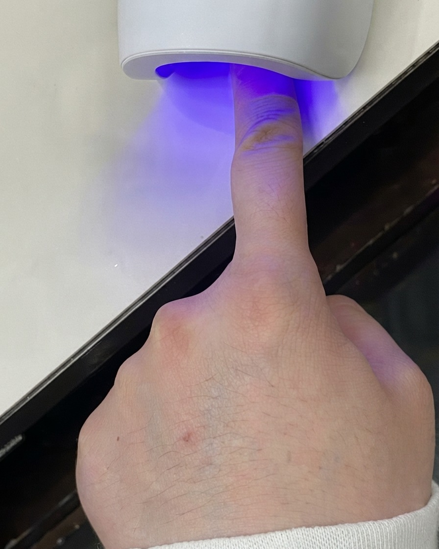 Un doigt placé sous une mini lampe UV LED pour catalyser la couche de gel.