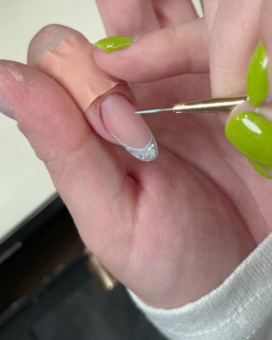Un ongle avec une délicate ligne de bordure bleue placé sous une mini lampe de catalysation LED.