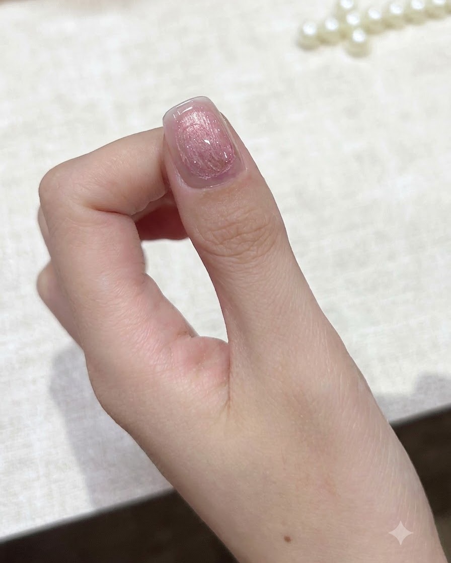 Un petit outil aimanté maintenu près dun ongle en gel rose cat-eye pour concentrer les particules scintillantes.