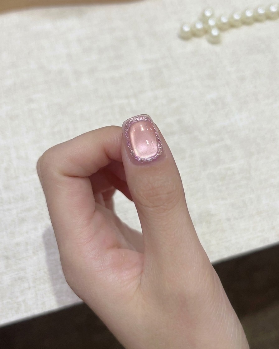 Un pinceau de détail fin appliquant un top coat transparent sur un ongle rose cat-eye poli.