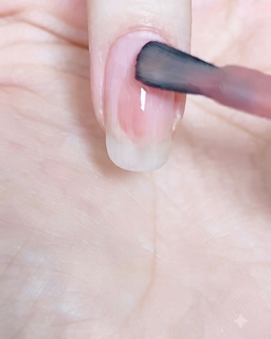 Un pinceau à ongle balayant le vernis rose vers le haut, en direction de la cuticule dun ongle naturel.