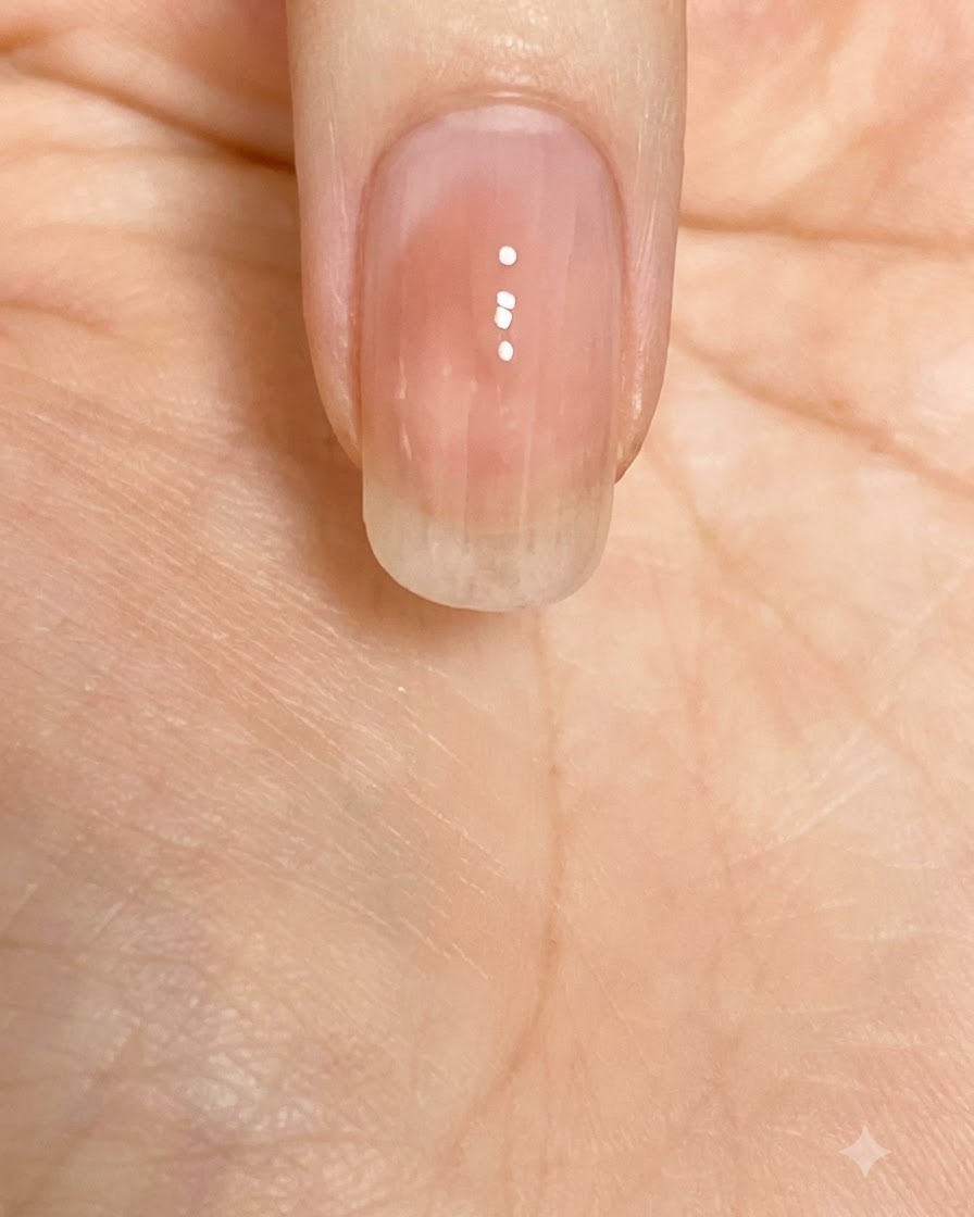 Un pinceau lissant le vernis rose vers le bas le long de la plaque de longle.