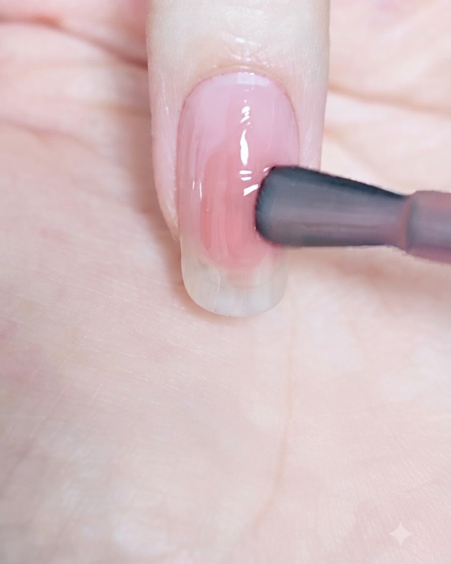 Un pinceau à vernis déposant une touche ciblée de rose plus soutenu au centre de longle.