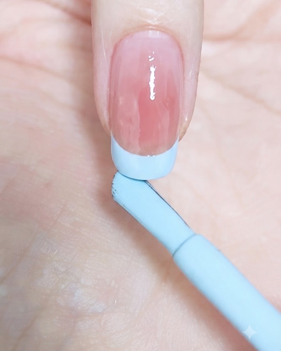 Gros plan sur un pinceau fin traçant le début dune French bleu pastel sur le côté gauche dun ongle naturel.