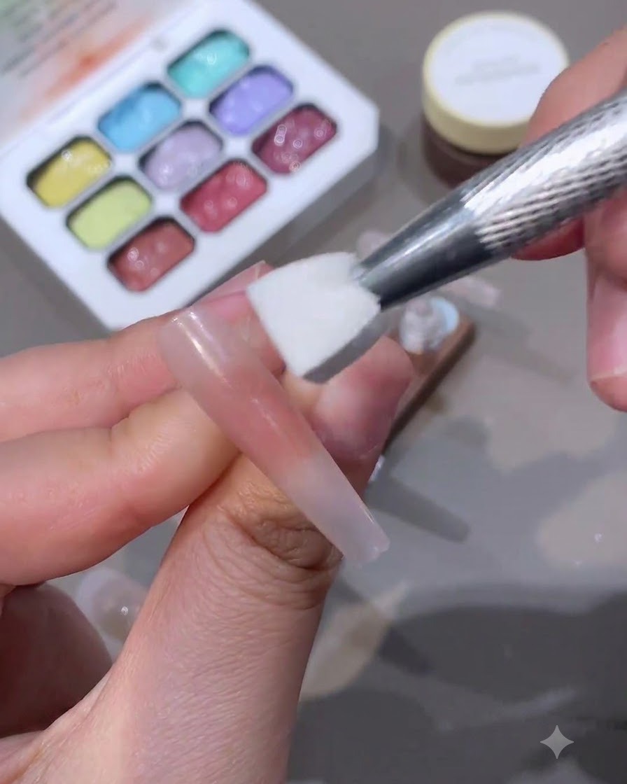 Un outil éponge appliquant une couleur blush au centre dun long onglet nude.
