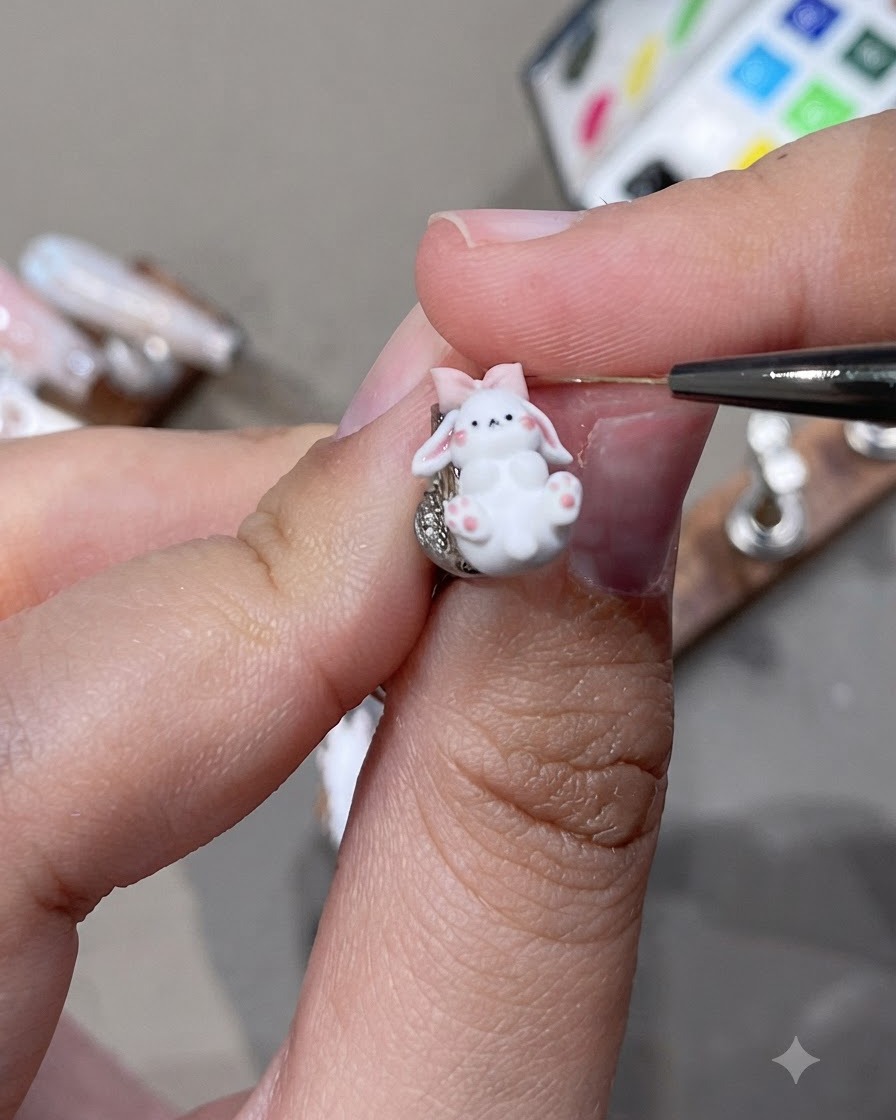 Un gros plan dun détail de charm dongle lapin 3D avec des oreilles roses et un petit nœud travaillé avec un outil fin.