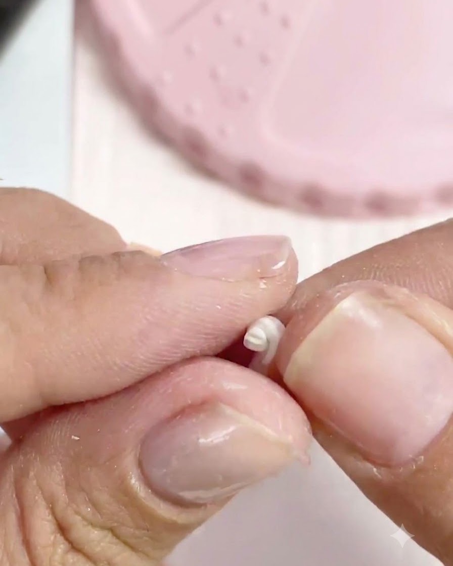 Des doigts roulant un minuscule morceau dargile blanche en une petite perle sphérique.