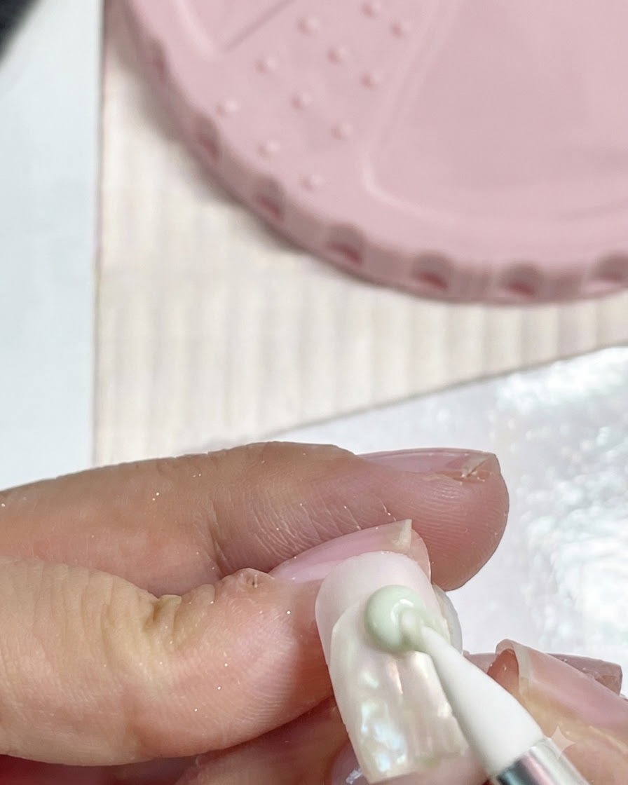 Un pinceau en silicone pour nail art pressant une petite perle dargile sur la surface dun ongle.