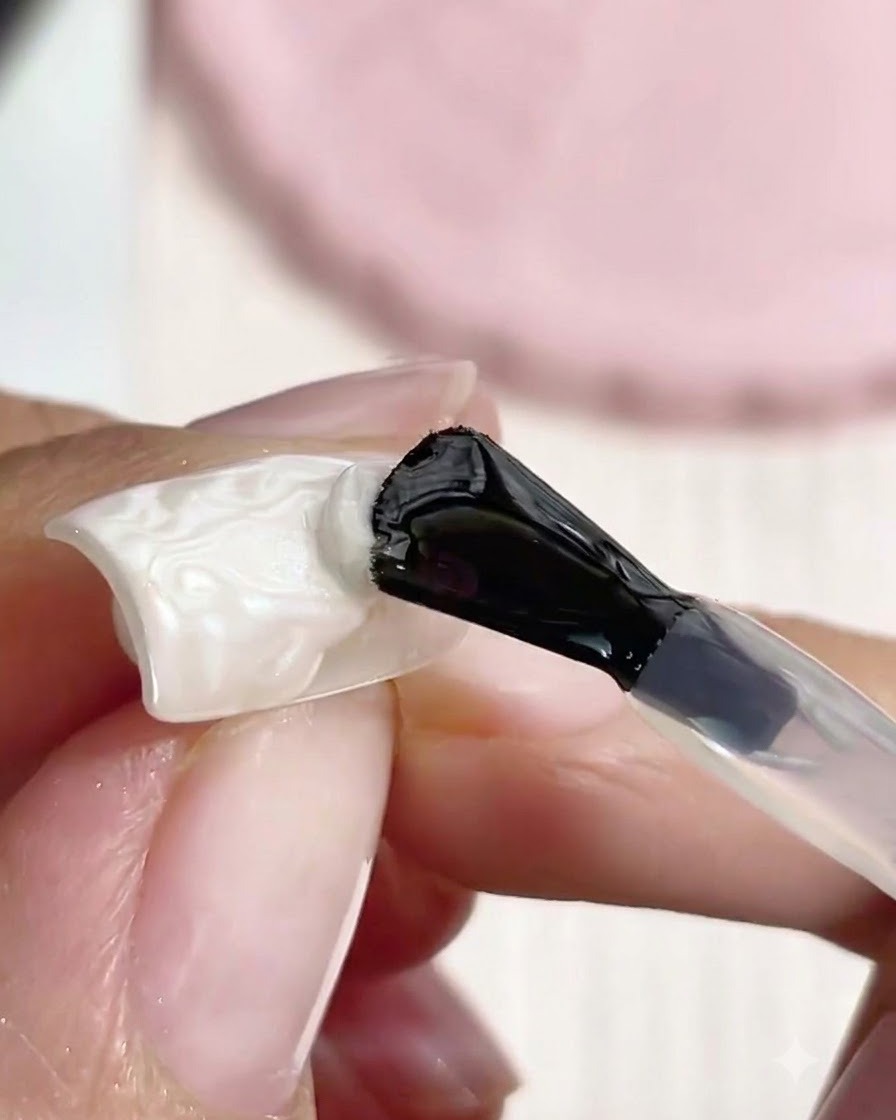 Un pinceau à manche noir appliquant un top coat transparent sur une perle texturée en 3D modelée pour le nail art.