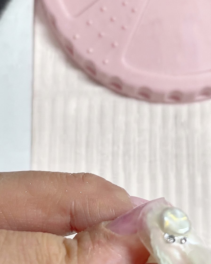 Vue rapprochée de petits cristaux argentés et de strass disposés proprement autour dun charm perle central sur un ongle.