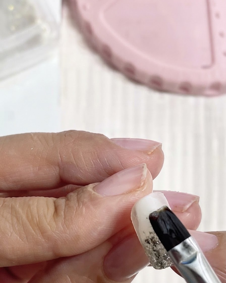 Un pinceau noir appliquant du gel de base le long du bord libre et des parois latérales dun ongle manucuré.